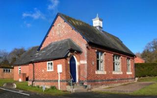 Red brick traditional village hall with gabled roof. Blue sky.