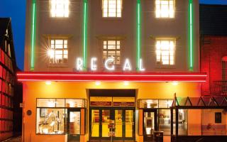Cinema exterior (signage: Regal) at night, lit up with green and red neon lighting 