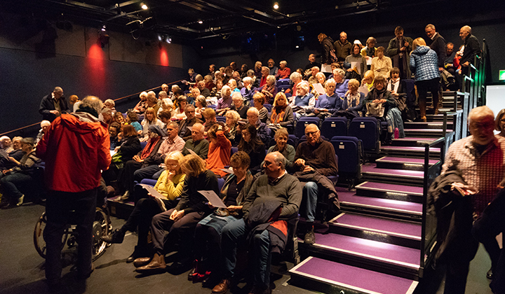 People entering a raked auditorium, wheelchair spaces in the front