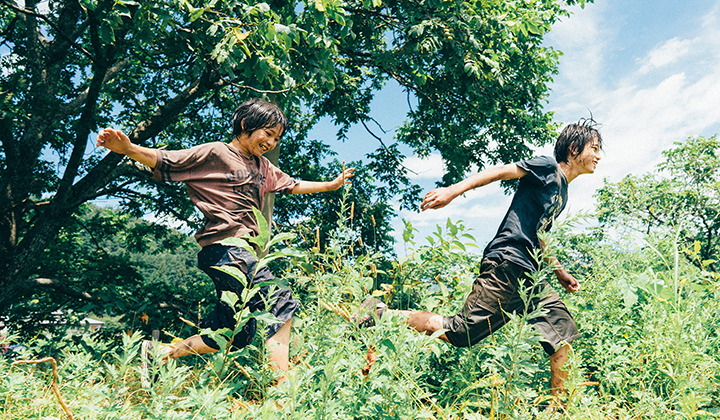Two south-east Asian boys running through long grass
