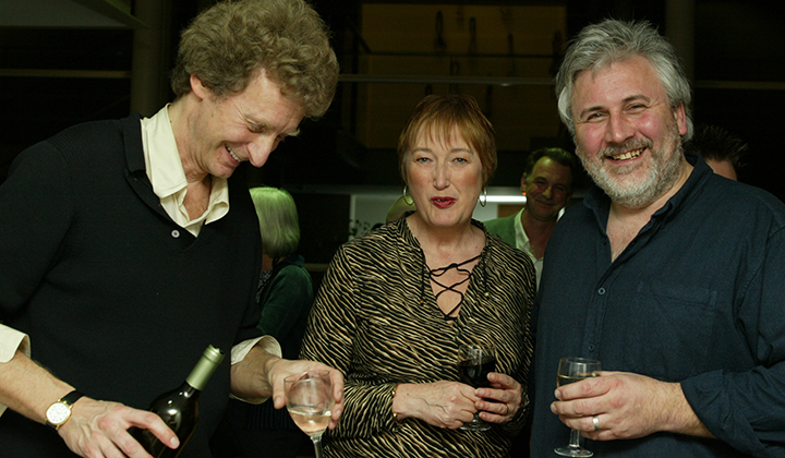 Smiling woman standing between two men, drinking wine