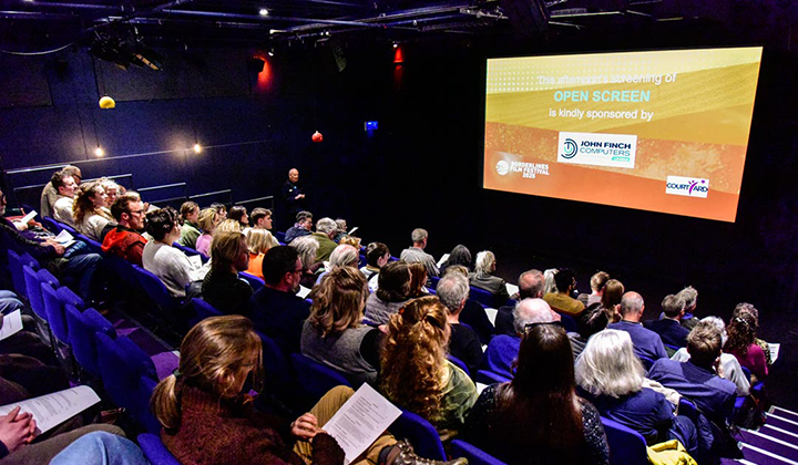 Auditorim with raked blue seating, orange slide reading Open Screen on screen.